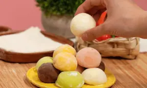 Bunte mochis eis in verschiedenen Geschmacksrichtungen auf einem gelben Teller. Eine Hand greift nach einem weißen mochi eis.