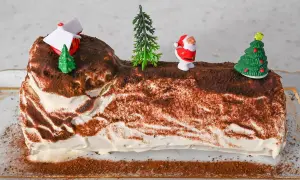 Eine festliche Bûche de Noël, dekoriert mit Weihnachtsmann, Bäumen und einem Haus.