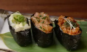 Drei leckere Sushi Gunkan mit Lachs, Garnelen und Fisch, garniert mit Frühlingszwiebeln und Kräutern.