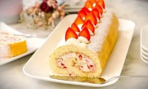 Ein köstlicher Brazo de Reina, gefüllt mit Sahne und Erdbeeren, dekoriert mit frischen Erdbeeren und Puderzucker.