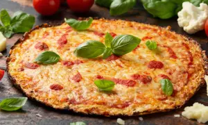 Eine köstliche blumenkohl pizza vegan, belegt mit Tomaten und Käse, garniert mit frischem Basilikum.