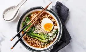 Schüssel mit japanischem Ramen, Nudeln, Ei, Gemüse und Tofuwürfeln, garniert mit Sesam und Schnittlauch.