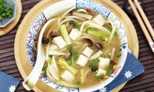 Herzhafte Miso Udon Suppe mit Tofu, Pilzen und Frühlingszwiebeln, serviert in einer dekorativen Schale.