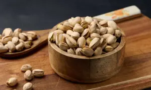 Schale voller Pistazien, bereit zum Backen mit Pistaziencreme. Ein Holzlöffel daneben ist ebenfalls gefüllt.