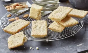 Goldbraune Financiers, frisch aus dem Ofen, warten auf das Financier Rezept. Mandeln liegen daneben.