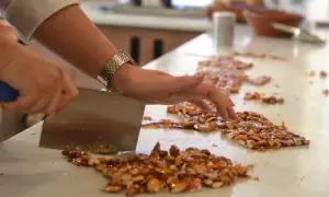 Eine Hand schneidet mit einem Messer karamellisierte Mandeln. So entsteht Nougat, das hauptsächlich aus Nüssen und Zucker besteht.