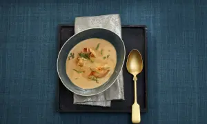 Eine Schüssel cremiger Hummerbisque mit Hummerstücken und Kräutern, daneben eine goldene Löffel.