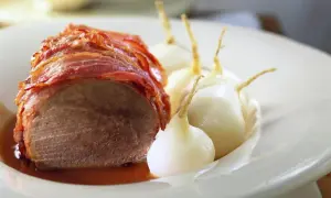 Boeuf à la mode: Ein saftiges Stück Rindfleisch, umwickelt mit knusprigem Speck, serviert mit kleinen, glasierten Zwiebeln in einer köstlichen Sauce.
