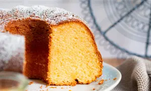 Saftiger Kuchen mit 12 Eiern, bestäubt mit Puderzucker, auf einem Teller mit einem Stück herausgeschnitten.