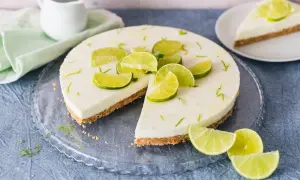 Erfrischender limetten cheesecake ohne backen, dekoriert mit frischen Limettenspalten und Zesten. Ein Stück ist bereits angeschnitten.