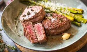 Zartes Filet de Boeuf, perfekt medium-rare gebraten, serviert mit grünem Spargel und einer Knoblauchzehe. Ein Festmahl!