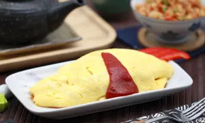 Ein leckeres Omurice Rezept: goldgelbes Omelett mit Ketchup-Streifen auf einem Teller, daneben eine Schüssel mit gebratenem Reis.