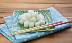 Würfel von daikon rettich auf einem grünen Teller, daneben Stäbchen auf einem blauen Tupftuch.