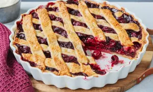 Ein frisch gebackener Kirschkuchen mit Gittermuster, perfekt für ein Kirschkuchen Rezept. Daneben eine Schüssel Schlagsahne.