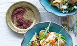 Gewürzschale mit rotem Pulver, vielleicht eine Sumach-Alternative, neben einem bunten Salat mit Blumenkohl und Ziegenkäse.