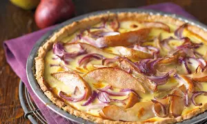 Herzhafte birnen quiche mit roten Zwiebeln und cremigem Guss, appetitlich in einer Metallform serviert.