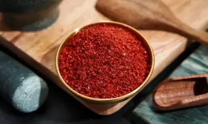 Schüssel mit leuchtend rotem Cayennepfeffer, bereit zum Würzen. Daneben ein Mörser und ein Holzschaber.