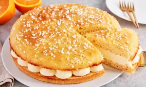 Eine köstliche Tarte Tropezienne, bestreut mit Zuckerperlen, gefüllt mit cremiger Vanillecreme. Daneben liegen Orangen.