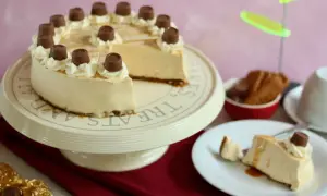 Eine köstliche karamell torte, verziert mit Sahnetuffs und Schokoladenstückchen, steht auf einem Tortenständer. Ein Stück ist bereits auf einem Teller angerichtet.