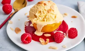 Ein Pfirsich Melba Rezept Original: Ein Pfirsich mit Vanilleeis, Himbeersauce und Mandelsplittern auf einem Teller, garniert mit frischen Himbeeren.