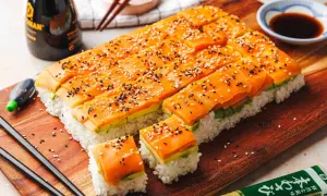 Leckere Sushi-Ideen: Reis, Avocado und Lachs, bestreut mit Sesam. Serviert auf einem Holzbrett mit Sojasauce und Wasabi.