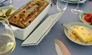 Fertige Terrine mit Speck und Lorbeerblättern, bereit für ein köstliches Terrinen Rezept. Dazu gibt es Butter, Radieschen und ein Glas Weißwein.