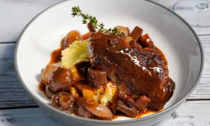 Ein authentisches Coq au Vin Rezept Original: zartes Hähnchen in Rotwein, serviert mit Kartoffelpüree, Speck und glasierten Zwiebeln.