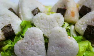 Herzförmige und dreieckige japanische Gerichte mit Reis, umhüllt von Nori-Algen, serviert auf knackigem Salat.