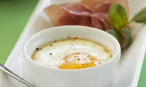 Ein köstliches oeuf cocotte mit einem perfekt gebratenen Ei, bestreut mit Pfeffer, serviert mit Schinken und Basilikum.