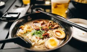 Herzhaftes Shoyu Ramen mit zartem Schweinefleisch, perfekt gekochtem Ei und Frühlingszwiebeln. Daneben ein kühles Bier.