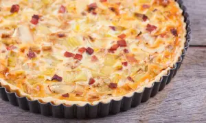 Eine herzhafte Quiche Lorraine mit Lauch und Speck in einer Metallform auf Holzhintergrund.