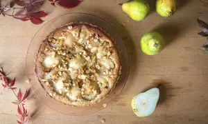 Eine köstliche Tarte Bourdaloue mit Birnen und Mandelsplittern, umgeben von frischen Birnen und herbstlichen Blättern auf Holzhintergrund.