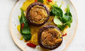 Zwei gefüllte Portobello Pilze auf gelben Ringen, garniert mit frischem Grün und Chilischeiben.