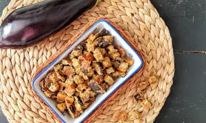 Knusprige, frittierte Aubergine in einer Schale, daneben eine ganze Aubergine. Ein leckerer Snack!