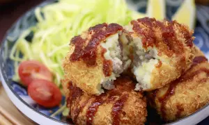 Knusprige japanische Kroketten, gefüllt mit Kartoffelpüree und Hackfleisch, serviert mit Salat und Tomaten.