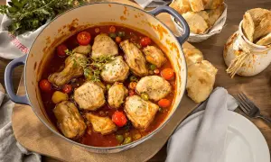 Herzhaftes Poulet Basquaise in einem Topf, mit Tomaten, Oliven und Kräutern, serviert mit Brot.
