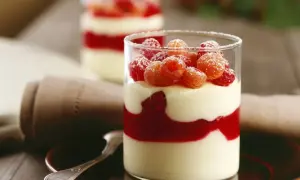 Zwei Gläser mit Schichten von Mousse au Chocolat Blanc, Himbeersauce und frischen Himbeeren, bestäubt mit Puderzucker.