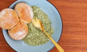 Drei Brötchen liegen auf einem Teller neben einer grünen Mischung, die zeigt, was ist schabzigerklee. Eine goldene Löffel liegt darin.