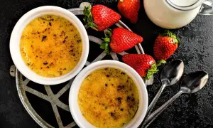 Zwei cremige Crème brûlée mit karamellisierter Zuckerkruste, garniert mit frischen Erdbeeren und einem Milchkännchen.