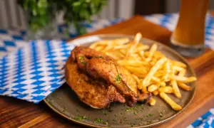 Ein knuspriger poulet roti mit Pommes Frites, garniert mit Kräutern, auf einem Teller mit blau-weiß karierter Serviette und einem Glas Bier.