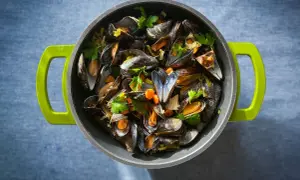 Ein Topf voller dampfender Moules Marinière, garniert mit frischer Petersilie und Karottenstücken, bereit zum Genuss.