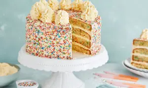 Eine leckere Torte mit weißem Zuckerguss und bunten Streuseln, gekrönt mit Sahnetuffs. Ein Stück ist angeschnitten und zeigt die saftigen Schichten.