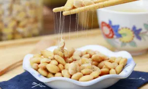 Fermentierte Sojabohnen, auch Natto genannt, werden mit Stäbchen aus einer Schale gehoben. Die klebrigen Fäden sind charakteristisch.