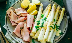 Ein Teller mit gekochtem Spargel, Schinken und Kartoffeln, garniert mit Petersilie. Perfekt für die besten Spargelrezepte!