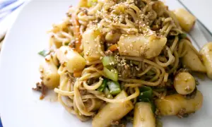 Yaki soba mit Hackfleisch, Möhren, Frühlingszwiebeln und Tteok (Reiskuchen), bestreut mit Sesam.
