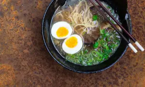 Schüssel mit dampfendem Ramen, zwei halbierten Eiern, Nudeln, Fleisch und Frühlingszwiebeln. Perfekt, um Ramen selbst zu machen!