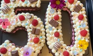 Ein aufwendig dekorierter Number Cake in Form der Zahl 50, verziert mit Sahnetuffs, Himbeeren, Schokolade und Blumen.