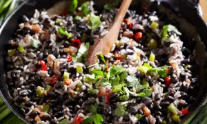 Reis mit schwarzer Bohne, Paprika und Chili in einer Pfanne, garniert mit Koriander. Ein Holzlöffel rührt die köstliche Mischung.