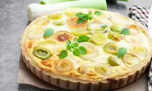Herzhafte Quiche aux poireaux mit goldbraunem Teig und frischen Lauchringen, garniert mit grünen Kräutern.