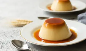 Zwei cremige flan kuchen mit flüssiger Karamellsoße auf weißen Tellern, daneben Löffel und ein paar Ähren.